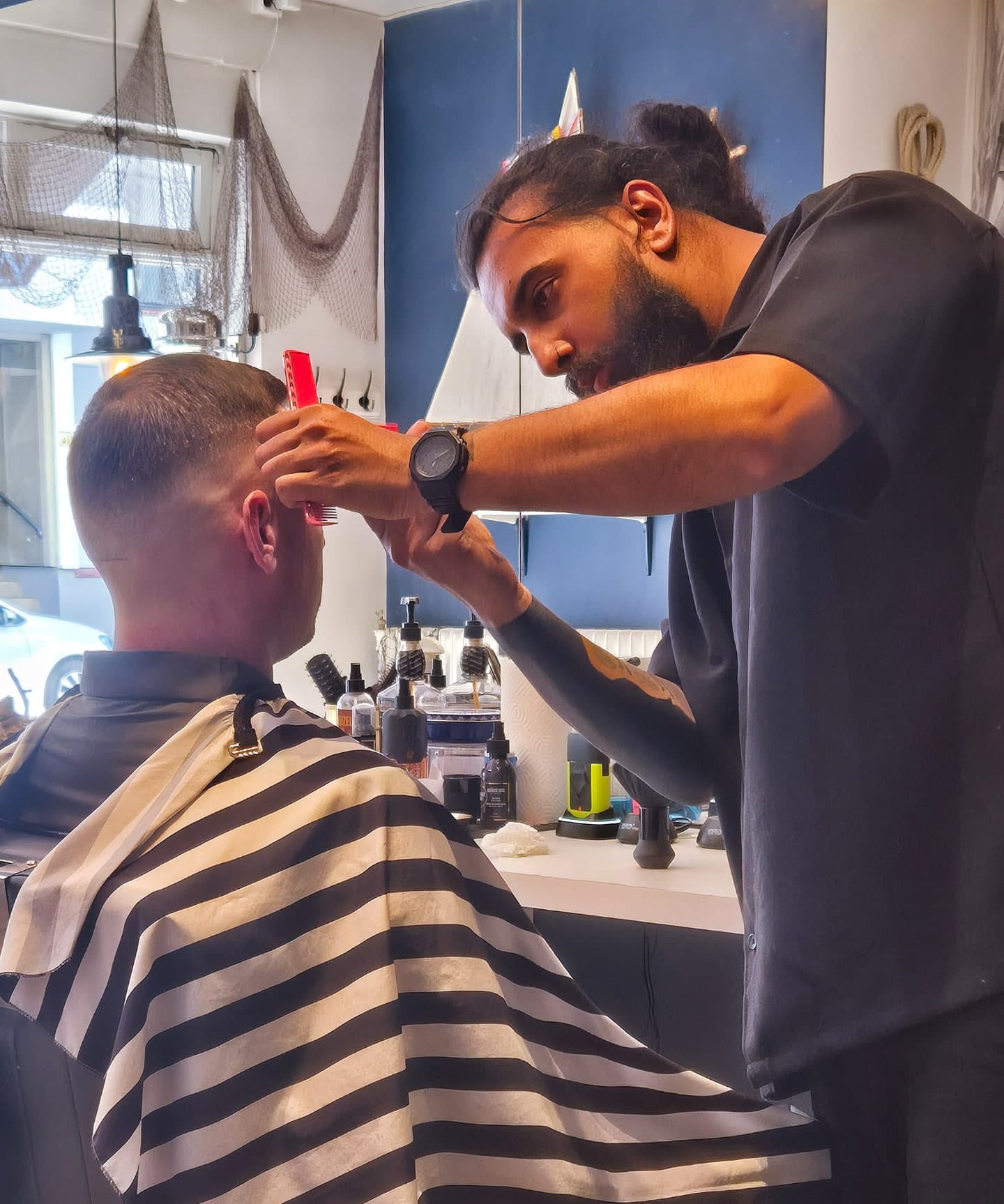 Barberer klipper en kunde inne på Old Sailor Barbershop, med tau og maritim dekor i bakgrunnen