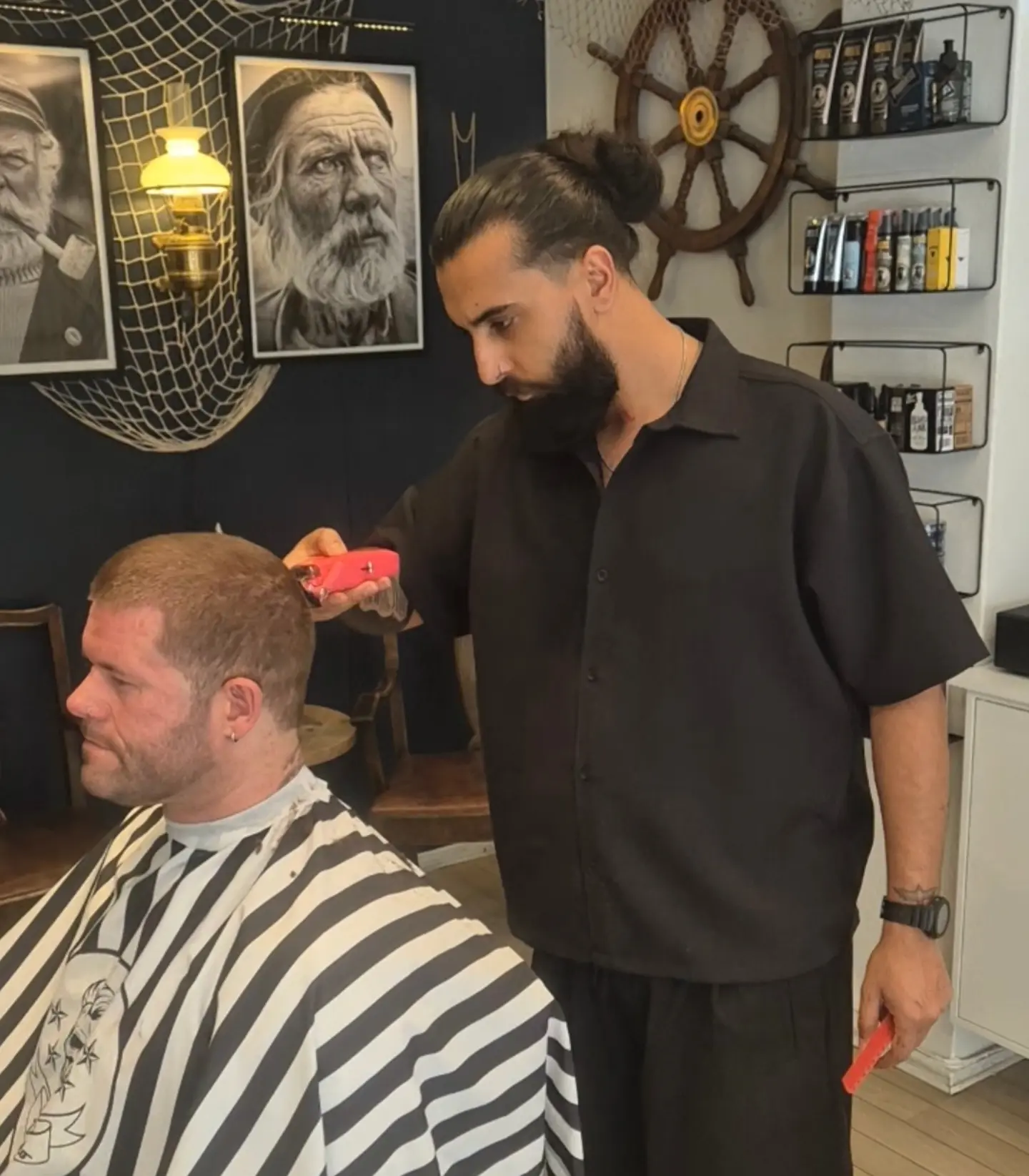 Barberer klipper en kunde med trimmer inne på Old Sailor Barbershop